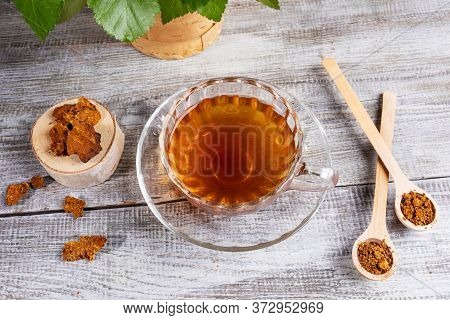 Healing Infusion Of Birch Mushroom Chaga In Figured Glass Cup And Chaga Pieces On Wooden Table. Tren