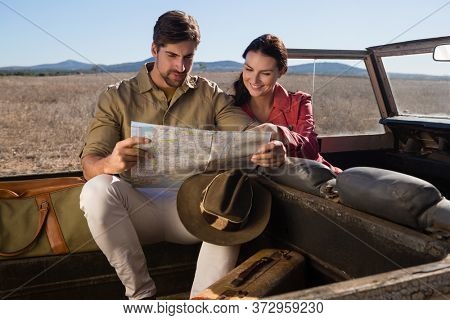 Smiling woman with man reading map in off road vehicle on landscape
