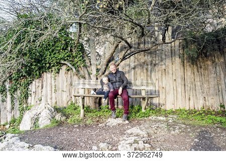 Father And Little Son Sitting On The Wooden Bench