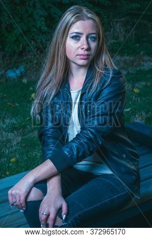 Nice Lady In Sad Mood Is Sitting On Parkbench And Looking At Camera.