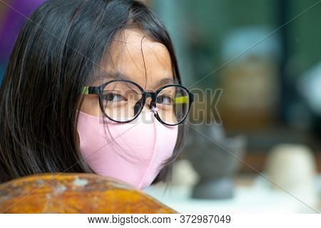 Closeup Face Of Young Girl Wearing Eyeglasses And Facial Mask With Hidden Smile Inside