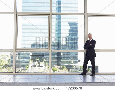 Retrato de longitud completa del empresario de seguros de mediana edad con los brazos cruzados pie por ventana en off