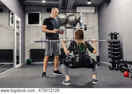 A Woman Exercising In An Electric Muscular Suit Stimulates Exercise In A Gym. A Young Female In An E