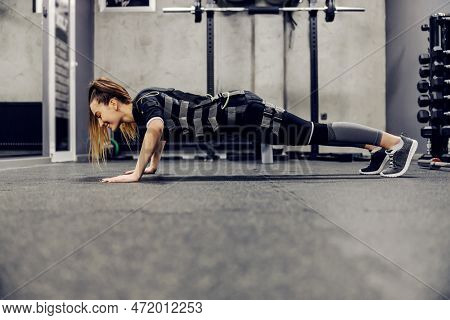 A Woman In A Black Ems Suit Lying Down In A Plank Position And Doing Push-ups In The Middle Of A Tra