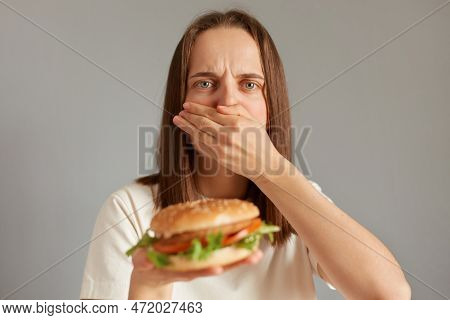 Indoor Shot Of Ill Woman Feeling Sick When See Fast Food, Covering Her Mouth Feels Nausea, Eating Sp