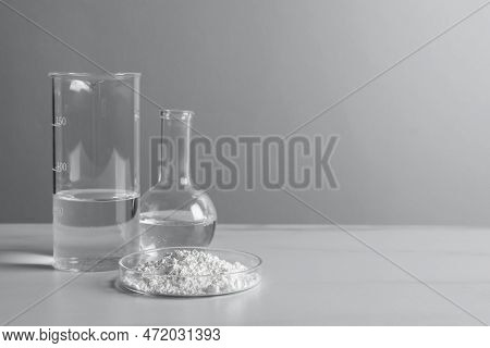 Petri Dish With Calcium Carbonate Powder And Laboratory Glassware On White Table. Space For Text