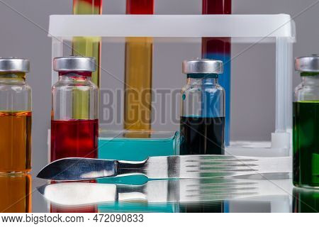Collection Of Drug Vials With Colored Solution. Sharp Mettalic Knife. Scientific Lab Medicine Resera