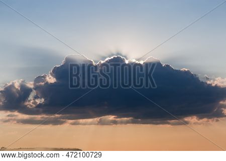 Section Of The Sky With Big Dark Cumulus Cloud And Sun Beams From Behind The Cloud Above The Distant