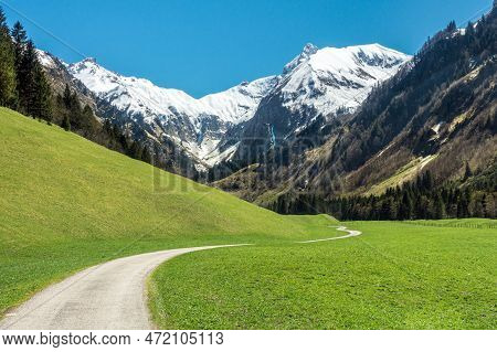 Beautiful Landscape With Snow Capped Mountains, Green Grass Meadows And Hiking Trail In Springtime. 