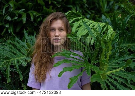 Portrait Of Young Woman Standing On An Ivy, Fern Wall Or In Greenery, Breathing, Smiling And Looking