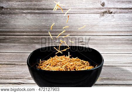 Close-up Of Cooked Polyphosphate Noodles Falling Into A Ceramic Bowl On A Wooden Table