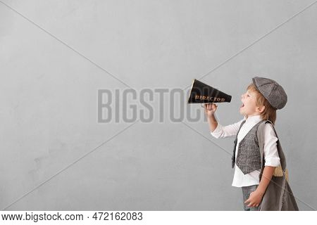 Newsboy Shouting Through Loudspeaker Against Grunge Wall Background. Kid Selling Newspaper. Child We