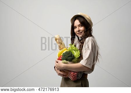 Portrait Of Happy Smiling Young Woman In Beige Oversize T-shirt Holding Reusable String Bag With Gro
