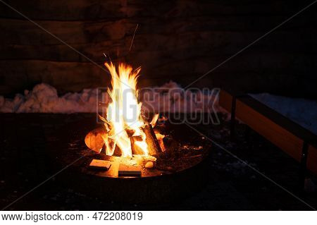 Firewood Burns In The Center Of A Round Metal Barbecue Table.