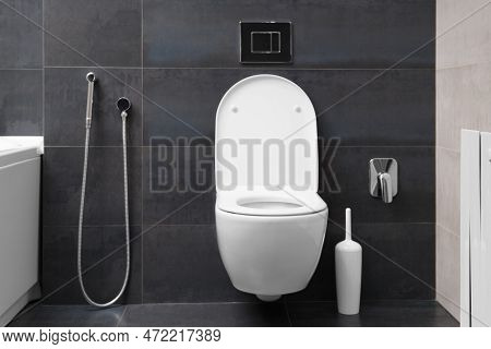Modern Wall-mounted White Toilet Bowl, Chrome Flush Button And Bidet Hygienic Shower Against The Bac