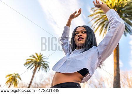 Young African Woman In White Clothes In A Tropical Location With Palm Trees At Sunset, Doing A Trend