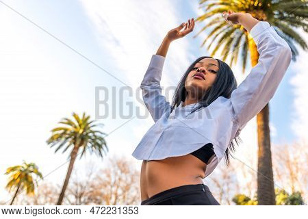 Young African Woman In White Clothes In A Tropical Location With Palm Trees At Sunset, Doing A Trend