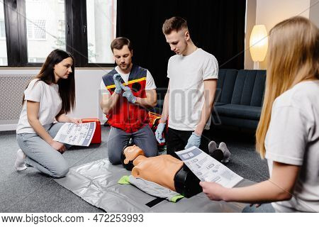 Young Man Instructor Helping To Make First Aid Heart Compressions With Dummy During The Group Traini