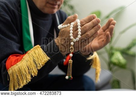 An Elderly Man Prays With A Rosary And The Flag Of The United Arab Emirates