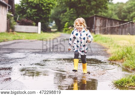 Little Toddler Girl Wearing Yellow Rain Boots, Running And Walking During Sleet On Rainy Cloudy Day.