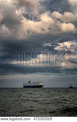 Large Ship Sails From The Port. Dramatic Clouds. Lighthouse. Vertical