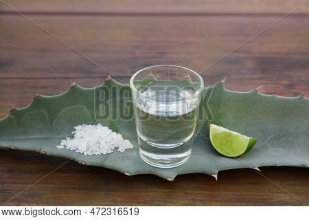 Mexican Tequila Shot, Salt, Lime Slice And Green Leaf On Wooden Table. Drink Made Of Agava