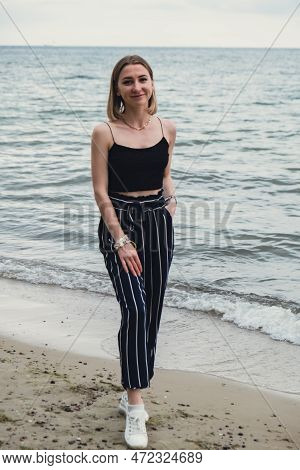 Young Woman Standing On Blurred Beachside Background. Attractive Female Enjoying Walking The Sea Sho