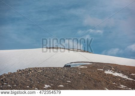 Dramatic Landscape With Huge Rock Mountain With Snowy Mountain Dome In Sunlight Under Clouds In Blue