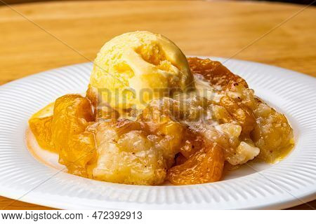 View Of Juicy Homemade Delicious Peach Cobbler With A Scoop Of Vanilla Ice Cream In White Ceramic Di