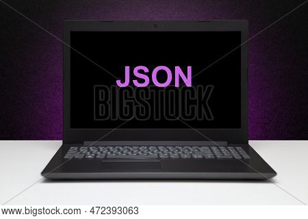 Json Text On Laptop Screen On Textured Black Background With Purple Light. Technology Concept.