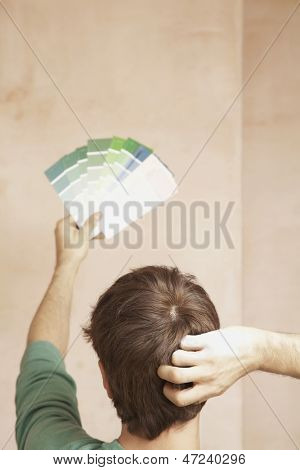 Rear view of man choosing color from swatches in unrenovated room