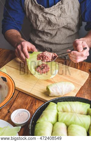 Man Cooking Cabbage Rolls Stuffed With Ground Meat In Kitchen