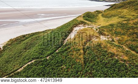 The Slope Of A High Hill On A Sandy Seashore. Green Grass Covered Mountain Beside Sea