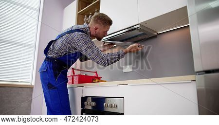 Young Handyman In Overall Fixing Kitchen Extractor Fan In Kitchen