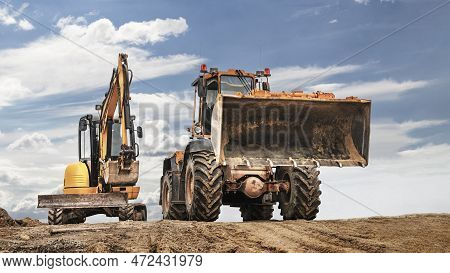 Powerful Wheel Loader Or Bulldozer Working And Mini Excavator Against Blue Cloudy Sky. Modern Equipm
