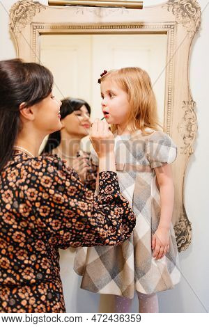 A Cute Little Girl In A Plaid Dress And Mom Primping.