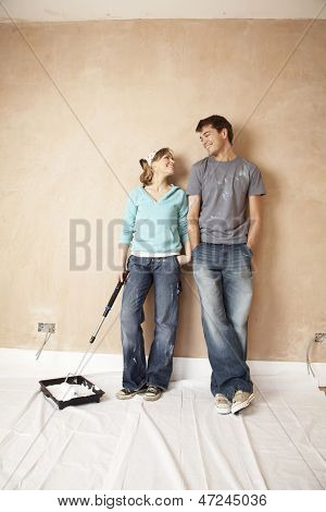 Woman dipping paint roller in paint while looking at man in unrenovated room