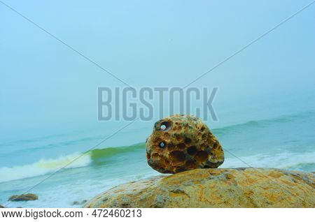 Large, Water-worn Stones Lay On A Rocky, Rugged Shoreline. The Ocean Churns In The Background And Sp