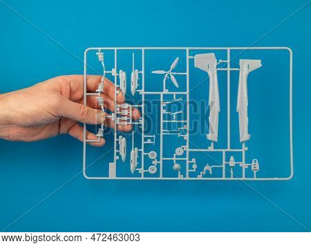 Sprue From A Plastic Model Kit In Hand On The Blue Background. Parts Tree Of The Airplane Model, Clo