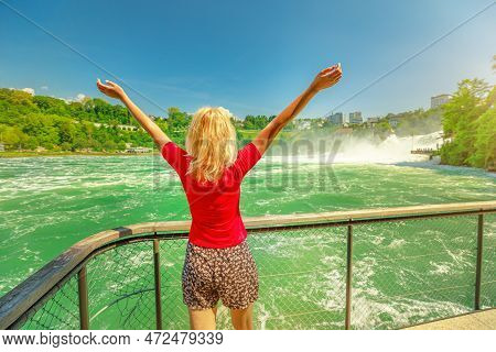 Girl With Open Arms Under The Rheinfall Waterfall Of Switzerland. Rhine Falls Are The Most Powerful 