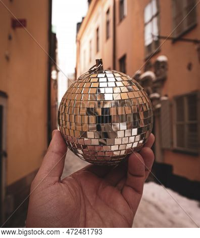 Cropped Hand Holding Disco Ball Admist Buildings