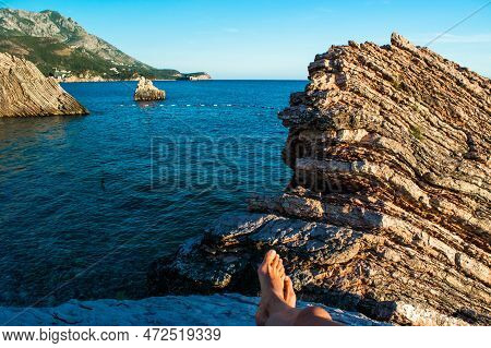 Legs Of Young Girl On Beautiful Rocks On Pebble Public Stone Beach. Rafailovici Esort Towns. Mounten