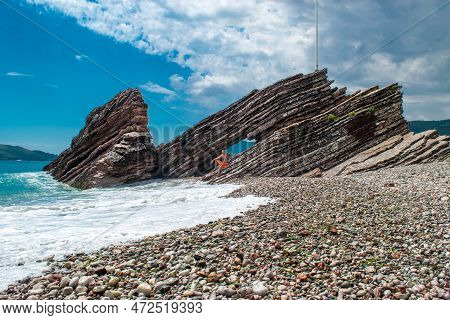 Young Man In Front Of Beautiful Rocks On Pebble Public Stone Beach. Rafailovici Esort Towns. Mounten