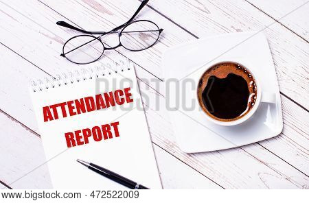 On A Light Wooden Background, Glasses, A Pen, A Cup Of Coffee And A Notepad With The Text Attendance