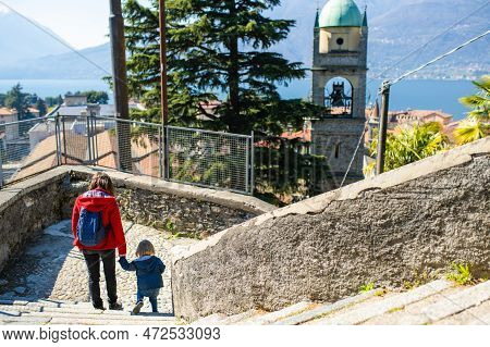 Mother And Toddler Son Exploring In Bellano Town, Located On The Eastern Shore Of Lake Como In The P