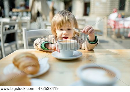 Cute Toddler Boy Having Hot Chocolate In Outdoor Cafe. Small Child Drinking Hot Beverage On Sunny Te
