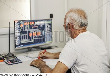 A Senior Operator Sitting In The Control Room And Looking At A Computer Monitor. Factory Worker Cont