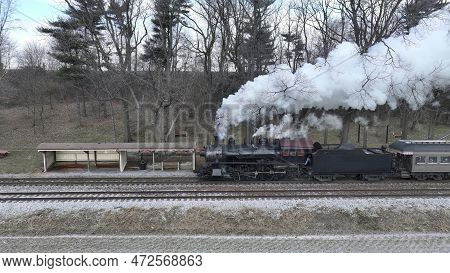 A Side Drone View Of A Steam Locomotive Approaching Traveling Thru Fields And Meadows, Blowing White