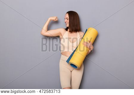 Portrait Of Confident Prod Woman Wearing Beige Top And Leggins Holding Fitness Mat Isolated Over Gra