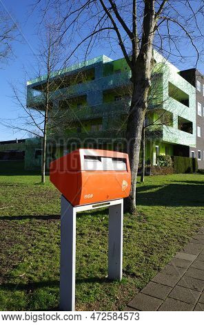 Beekbergen, Netherlands - Feb 28 2023 An Orange Mailbox In Front Of A Modern Green Apartment Buildin